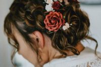 a wedding low updo with large braids on the sides, with locks down and white and red blooms tucked in