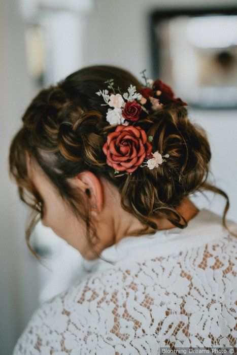 a wedding low updo with large braids on the sides, with locks down and white and red blooms tucked in