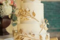 a white textural wedding cake with gilded leaf branches and white and pink roses on top