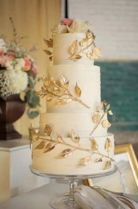 a white textural wedding cake with gilded leaf branches and white and pink roses on top