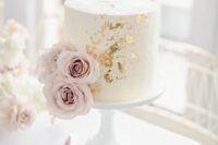 a white wedding cake decorated with gold leaf and pale pink roses is a chic idea for a wedding with a touch of glam