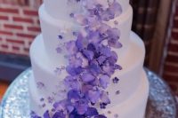 a white wedding cake decorated with white to deep purple blooms and smaller sugar blooms is a bold and contrasting color statement