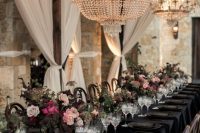 an elegant and opulent Halloween wedding table with a black tablecloth, plates, menus, blush and pink blooms and greenery