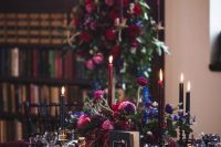 an exquisite Halloween wedding tablescape with a navy tablecloth, purple napkins, a lush centerpiece of purple, pink and burgundy blooms and bloody candles