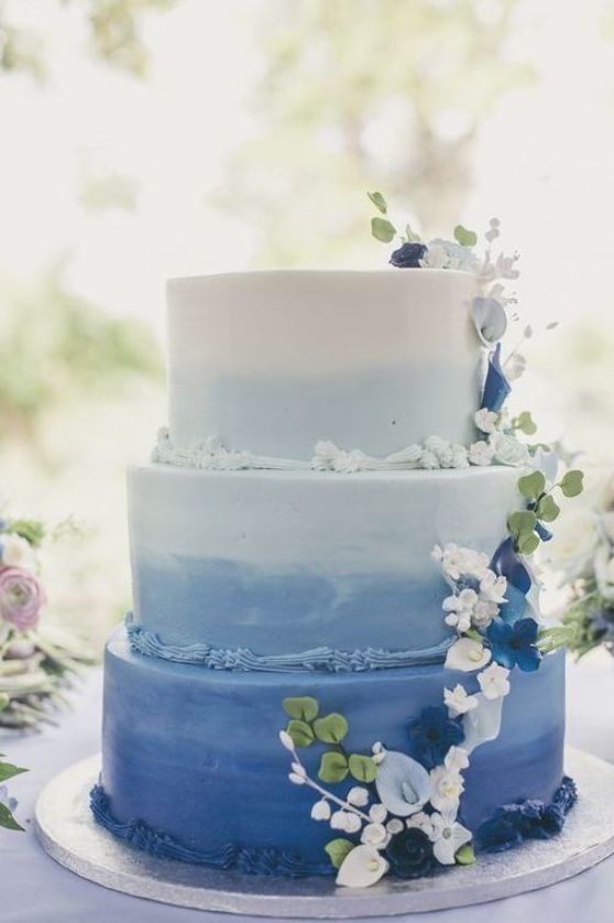 an ombre blue wedding cake with sugar detailing, white and blue blooms and leaves is a bold and catchy idea for a bright summer garden wedding