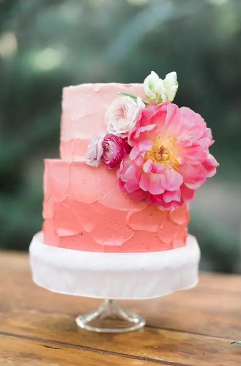 an ombre coral pink textural buttercream wedding cake decorated with white and hot pink blooms and a bit of greenery will fit a colorful spring or summer wedding