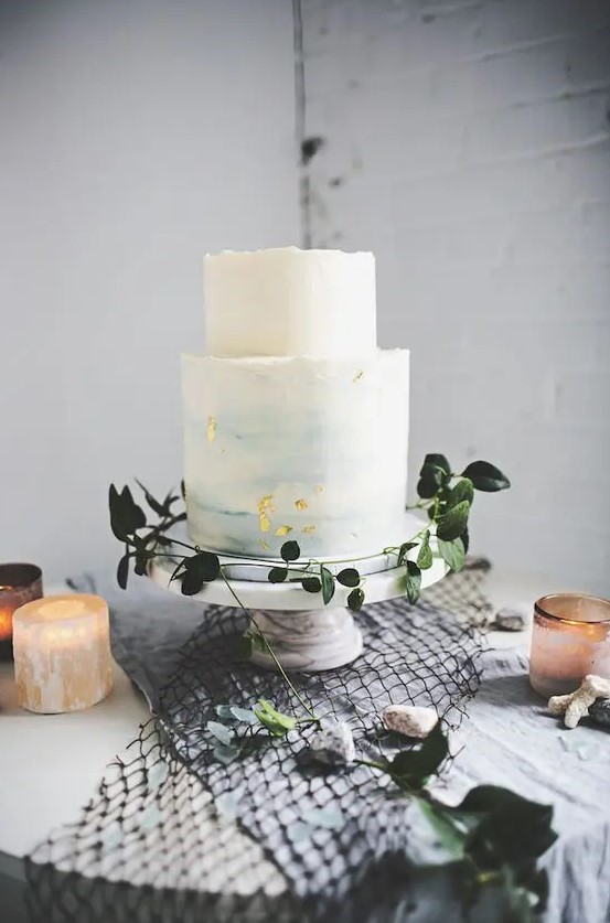 an ombre light blue wedding cake with a raw edge and gold leaf for a seaside wedding