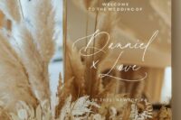 beautiful glam and white wedding decor with a polished gold sign with calligraphy, an arrangement of neutral blooms and pampas grass