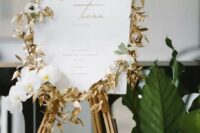 wedding signage with gilded foliage, white orchids and gold printing is a very refined and beautiful idea