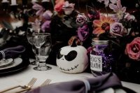 a beautiful Halloween wedding centerpiece of lilac and pink blooms, dark foliage, a skeleton pumpkin and some candles