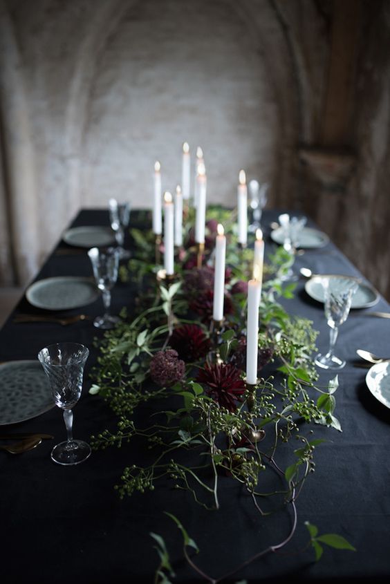 a beautiful and textural wedding table garland of lush greenery and deep burgundy blooms plus tall and thin candles