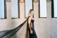 a black mermaid wedding dress with lace inserts on the sides and a long cape