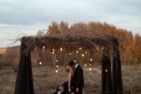 a black wedding arch with fabric, dried branches and bulbs hanging down