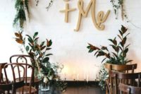a boho indoor wedding backdrop with a greenery, grass and bloom wedding arch, letters and branch arrangements and candles on the floor