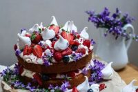 a bold naked sponge cake with strawberries, raspberries, meringues and purple flowers for a mid-summer wedding