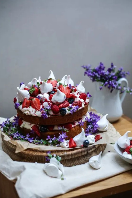 a bold naked sponge cake with strawberries, raspberries, meringues and purple flowers for a mid-summer wedding