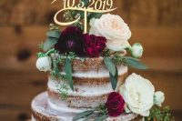a bold naked wedding cake with neutral and burgundy blooms, with greenery and a calligraphy topper for a summer wedding