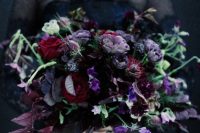 a catchy Halloween wedding bouquet in purple, burgundy, blue, with dark foliage, greenery and much texture