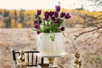 a centerpiece composed of a white pumpkin vase with purple tulips and gilded skull towers is a great idea for Halloween, and stacked gilded skulls add chic to it