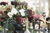 a chic Halloween wedding centerpiece of white and deep burgundy blooms, greenery, berries and leaves plus a candelabra