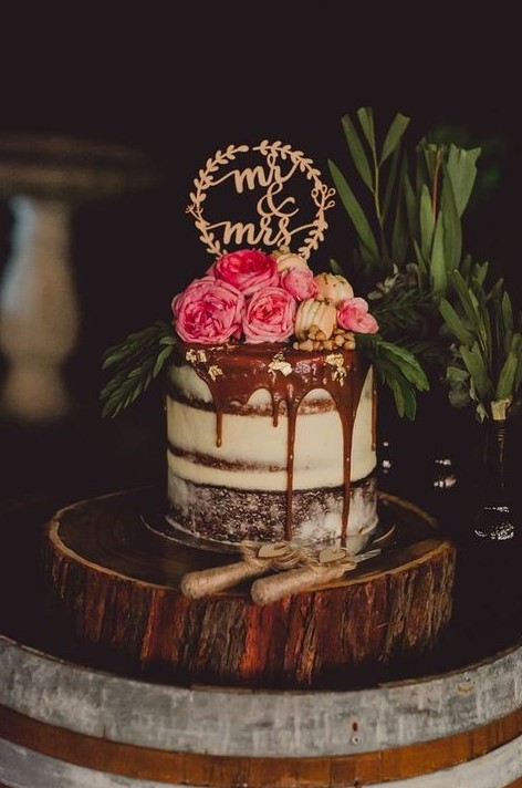 a chocolate drip naked wedding cake with fresh flowers, macarons, greenery and an elegant topper looks chic and yummy
