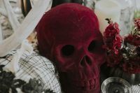 a cluster wedding centerpiece of a burgundy plush skull, a pumpkin planter with a succulent, a white pumpkin in black lace and antlers