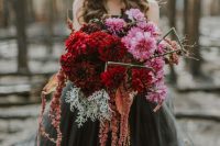 a colorful and textural wedding bouquet of pink, red and rust cascading blooms, pale millet and stems to stand out with a black wedding dress