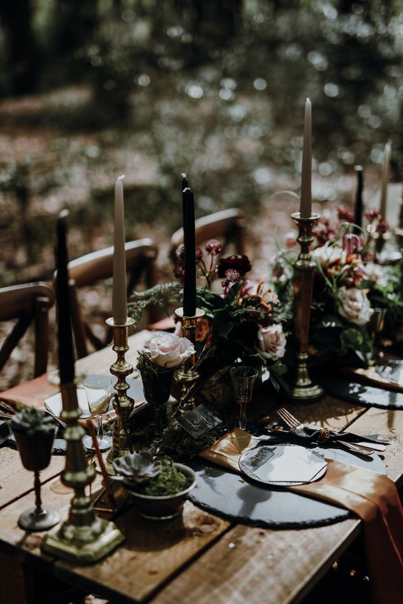 a dark tablescape with an uncovered table, succulents, blooms, greenery and white and black candles