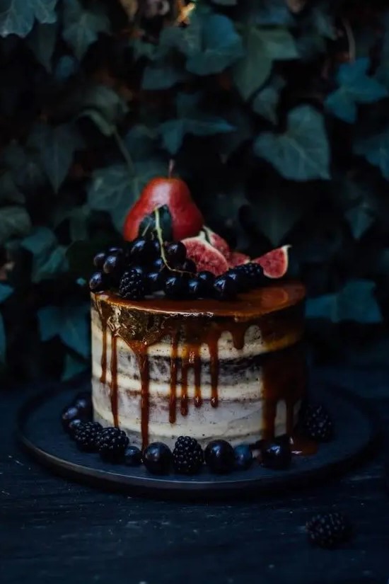 a decadent semi naked wedding cake with caramel drip, berries, pears and figs on top for fall