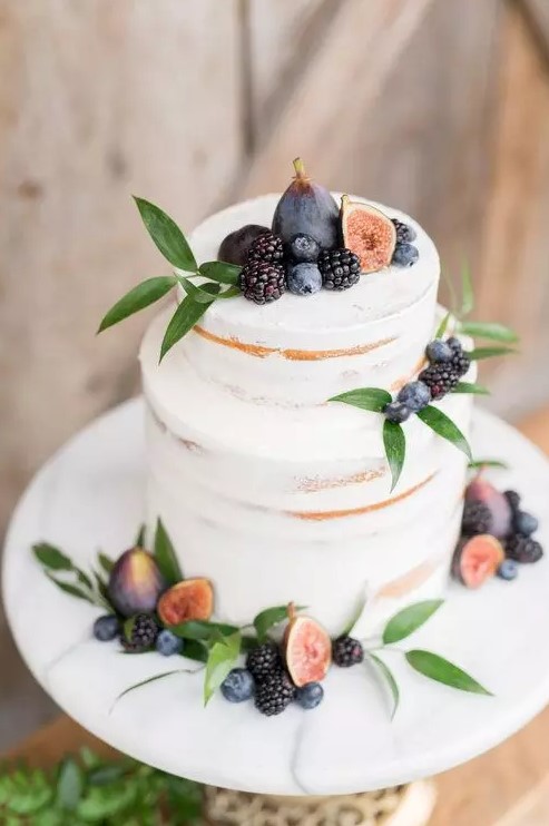 a delicate and pretty fall vineyard wedding cake   a semi naked piece topped with fresh greenery, figs, blackberries and blueberries