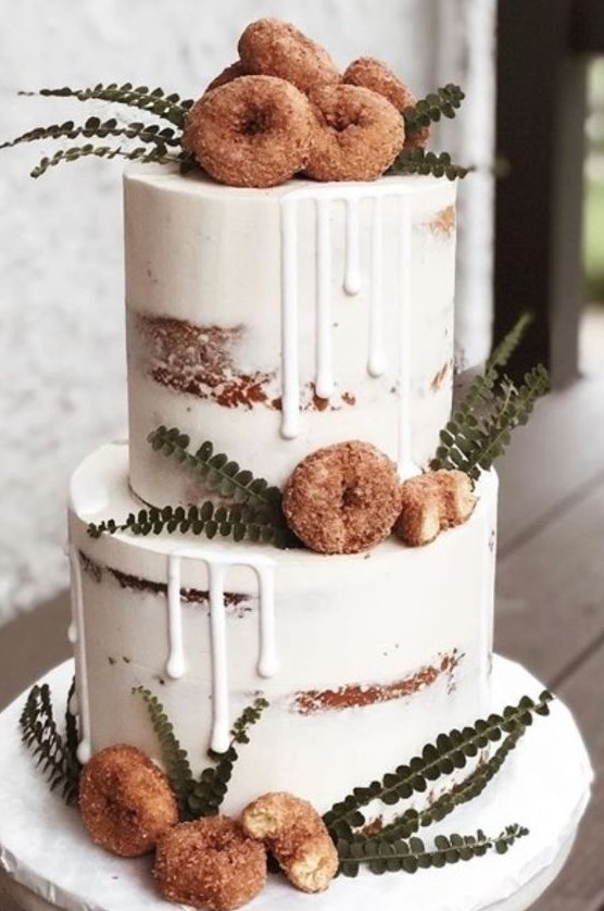 a delicious looking naked two tier wedding cake with creamy drip, crusty donuts and greenery is a very chic and lovely idea