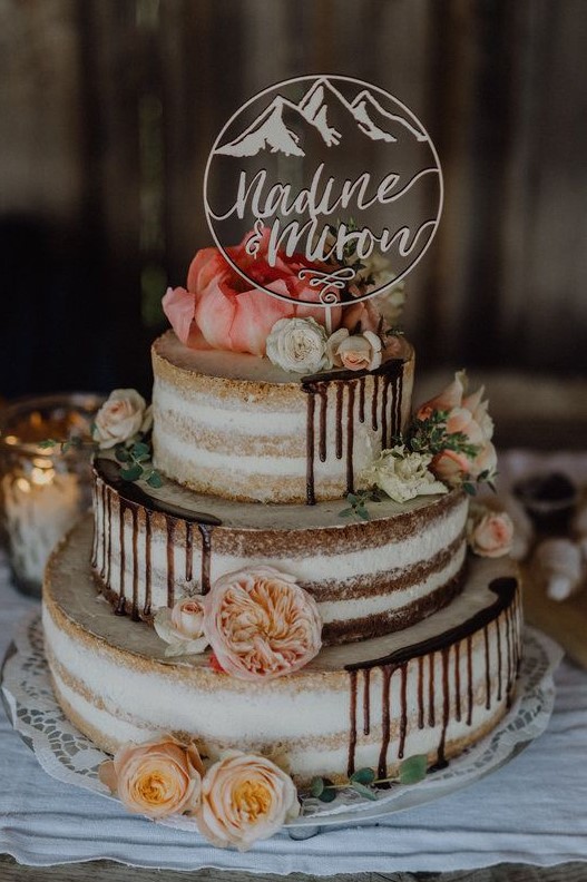 a delicious three tier naked wedding cake with chocolate drip, neutral and pastel blooms and a mountain topper