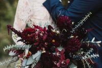 a fantastic bold Halloween wedding bouquet with burgundy and dark pink blooms, greenery with much texture and dark ribbons