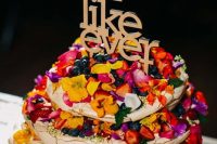 a fantastic pavlova wedding cake with bold edible flowers, petals, fresh berries and fruits and a lovely gold topper