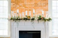 a faux fireplace decorated with greenery and bold blooms, lots of candles in candle holders and lanterns
