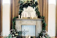 a faux fireplace with candles, greenery and white blooms plus candles on the floor and mantel