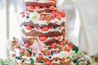 a gorgeous naked wedding cake with fresh bberries and white and pink blooms, with greenery is a lovely idea for a summer boho wedding