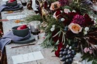 a gothic forest tablescape with an uncovered table, grey plates and chargers, lush blooms and greenery plus berries and black candles
