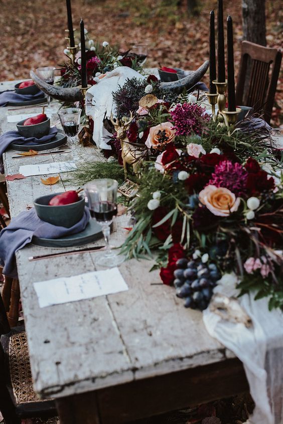 a gothic forest tablescape with an uncovered table, grey plates and chargers, lush blooms and greenery plus berries and black candles
