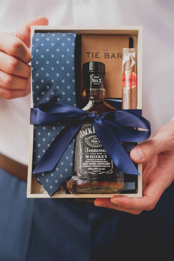 a groomsmen gift box with a tie, a bottle of whiskey, a cigar and a notebook is a stylish and easy idea