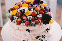a lovely and bright pavlova wedding cake with berries, fruits and colorful edible blooms is a splash of colors and gorgeousness