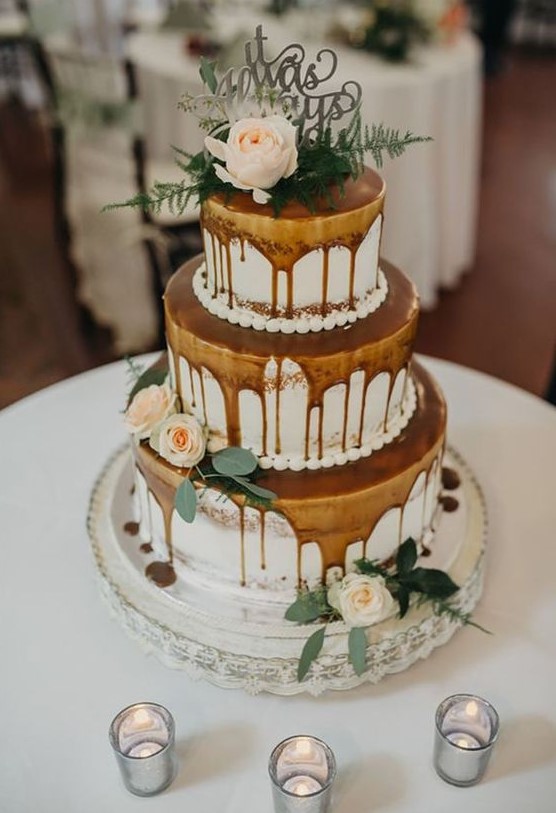 a lovely three tier naked wedding cake with caramel drip, neutral blooms and greenery and a silver topper is a chic dessert