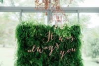 a lush greenery wall with a quote in copper letters and refiend copper chandeliers over the wall is a cool way to feel outdoors while being indoors