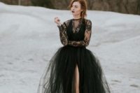 a modern black wedding dress with a lace top, a tulle skirt with a front slit and long sleeves, black shoes and a moody lipstick