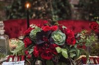 a moody Halloween centerpiece with red roses, greenery, dark foliage and cabbage plus a moss table cover
