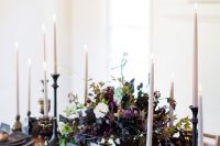a moody centerpiece with a black bowl with greenery, dark foliage, purple and blush blooms and much texture
