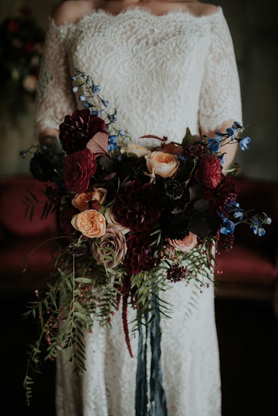 a moody wedding bouquet with burgundy, red, black and peachy blooms, touches of blue, berries, leaves and blue ribbons