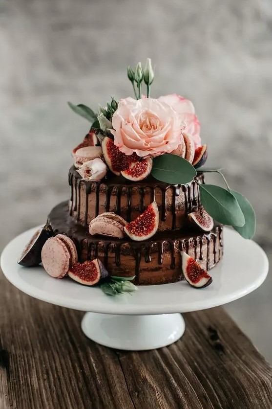 a naked chocolate wedding cake with chocolate drip, pink macarons, blooms, greenery and fresh figs is a delicious-looking and lovely idea for a wedding