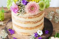 a naked wedding cake topped with greenery and bright flowers is a nice idea for a colorful spring or summer wedding