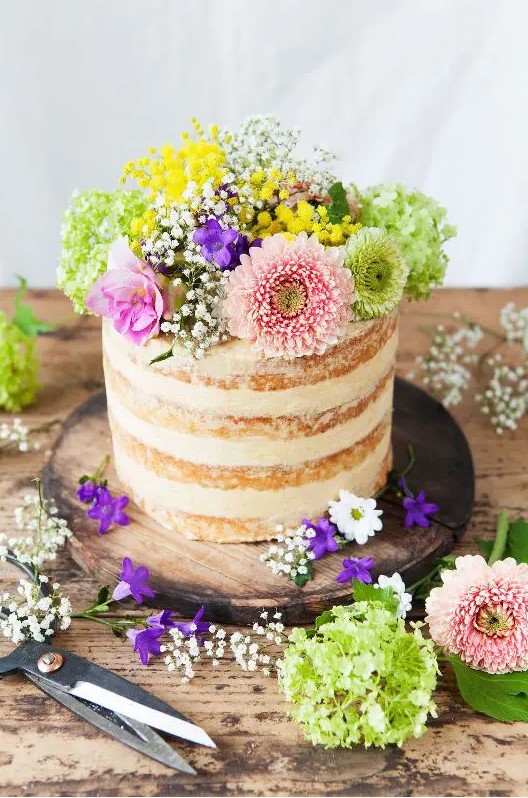 a naked wedding cake topped with greenery and bright flowers is a nice idea for a colorful spring or summer wedding